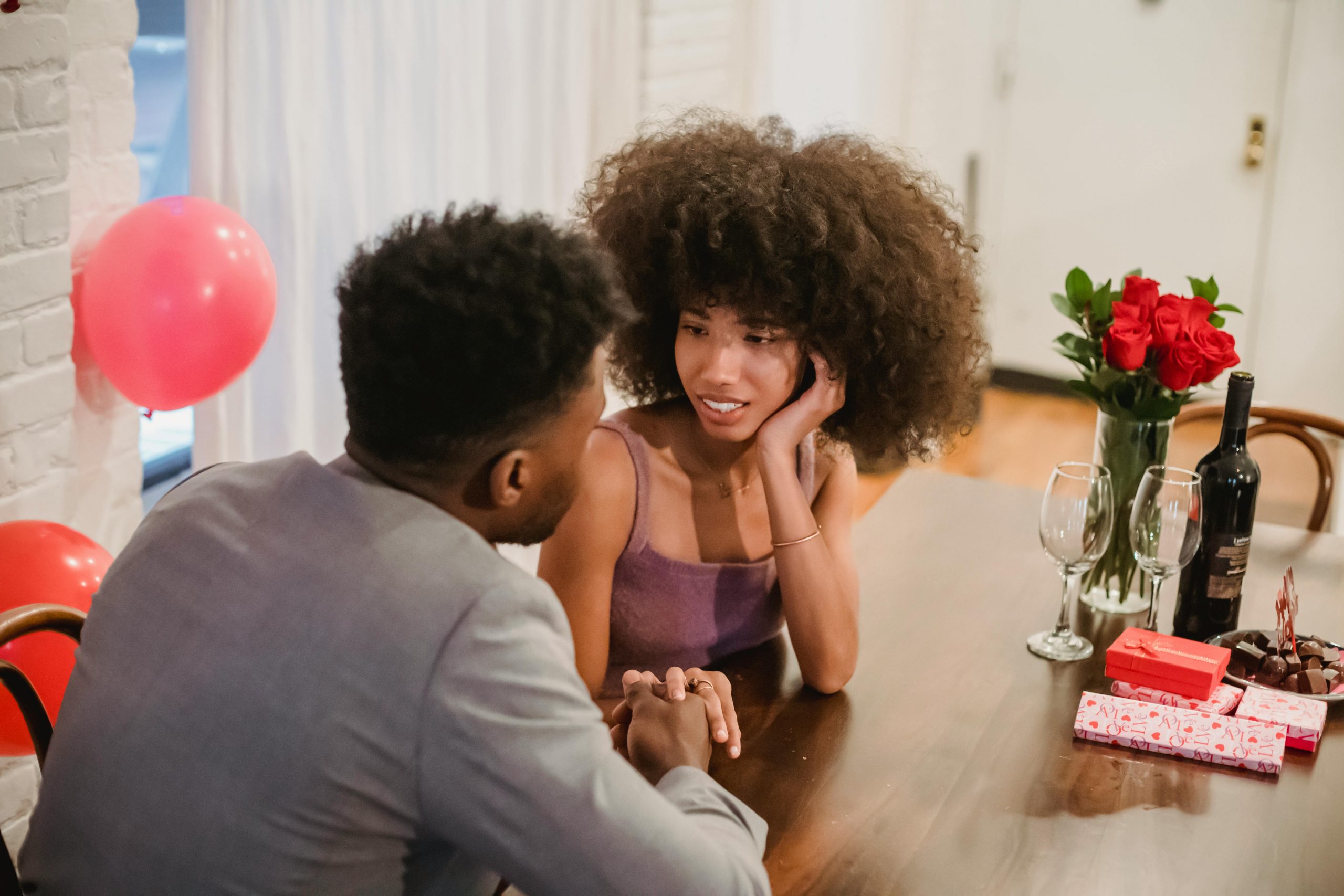 couple sharing a heartfelt conversation at a table set with a wine bottle, glasses, and roses