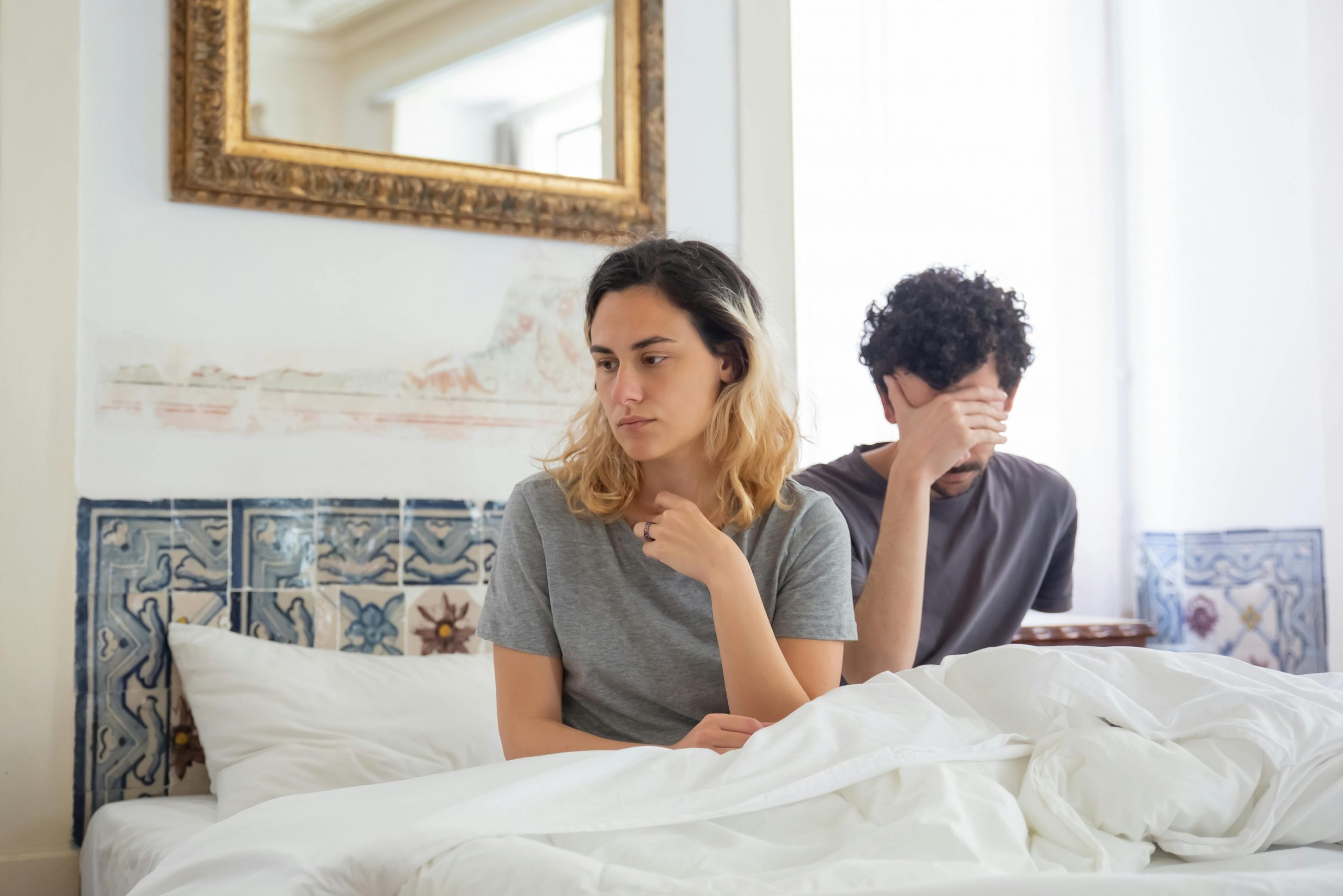 tired-looking couple sitting apart in bed