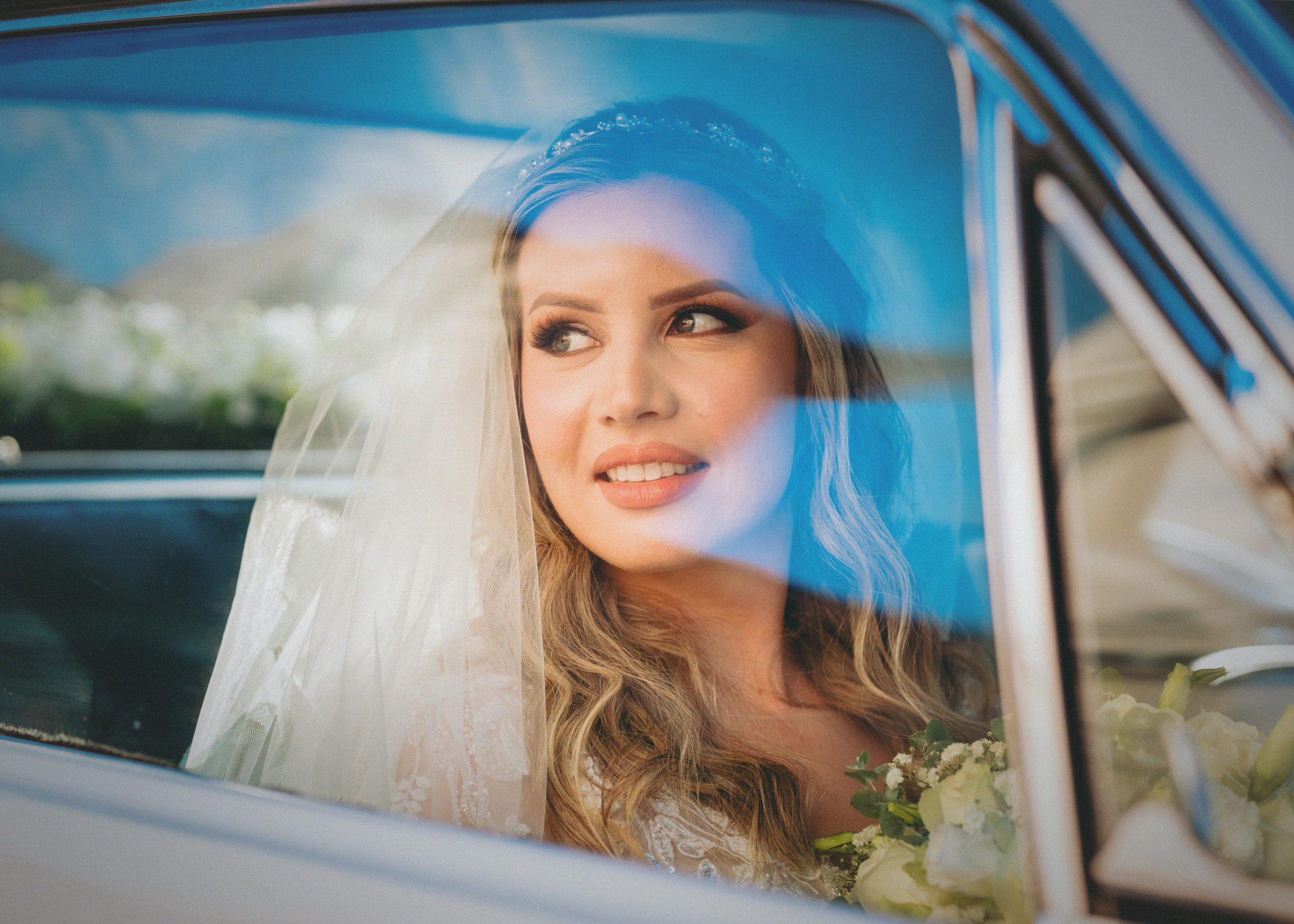bride with natural makeup smiling and looking out the window of a car